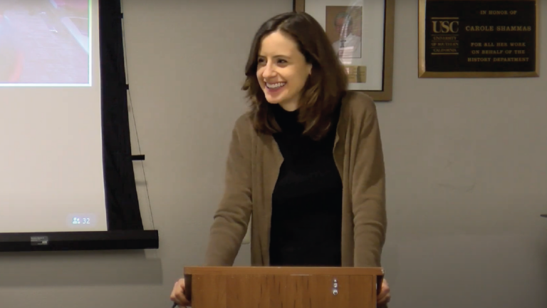 Charlotte Kiechel looks off to the left from behind a podium, smiling.