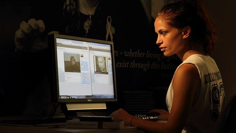 A white woman looks at the USC Shoah Foundation's Visual History Archive on a computer screen. The photo is dramatically lit.