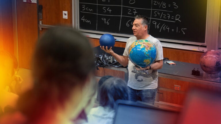 Faculty member talking in front of lecture hall. Holding 2 globes in his hand
