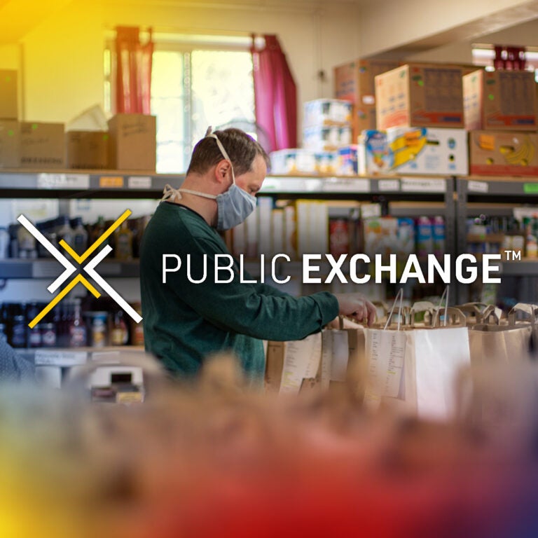man in food bank sorting through items with full shelves behind him. Public Exchange Logo in the front of the image
